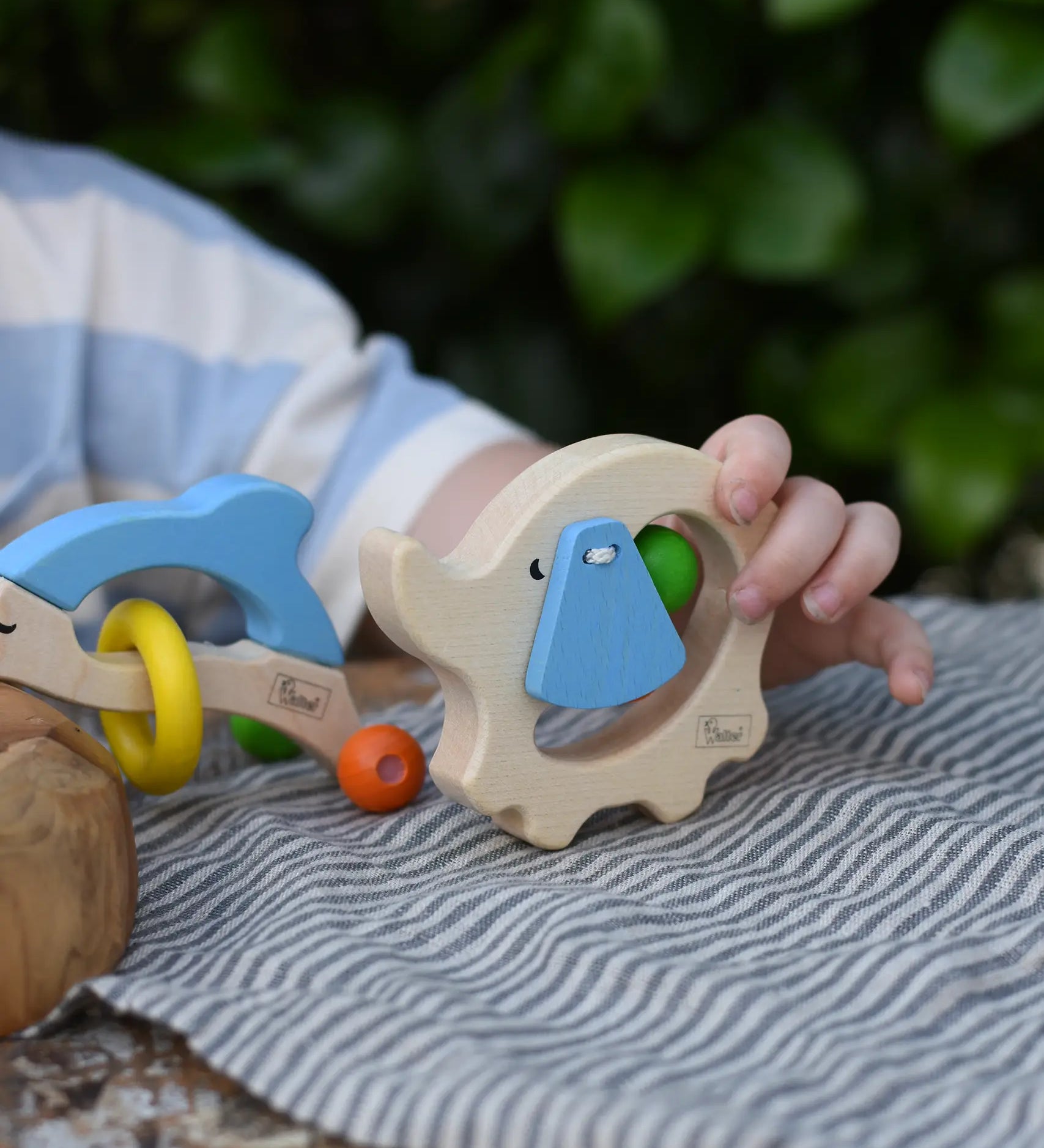 Child holding the back of the Nic elephant grasper wooden baby toy.