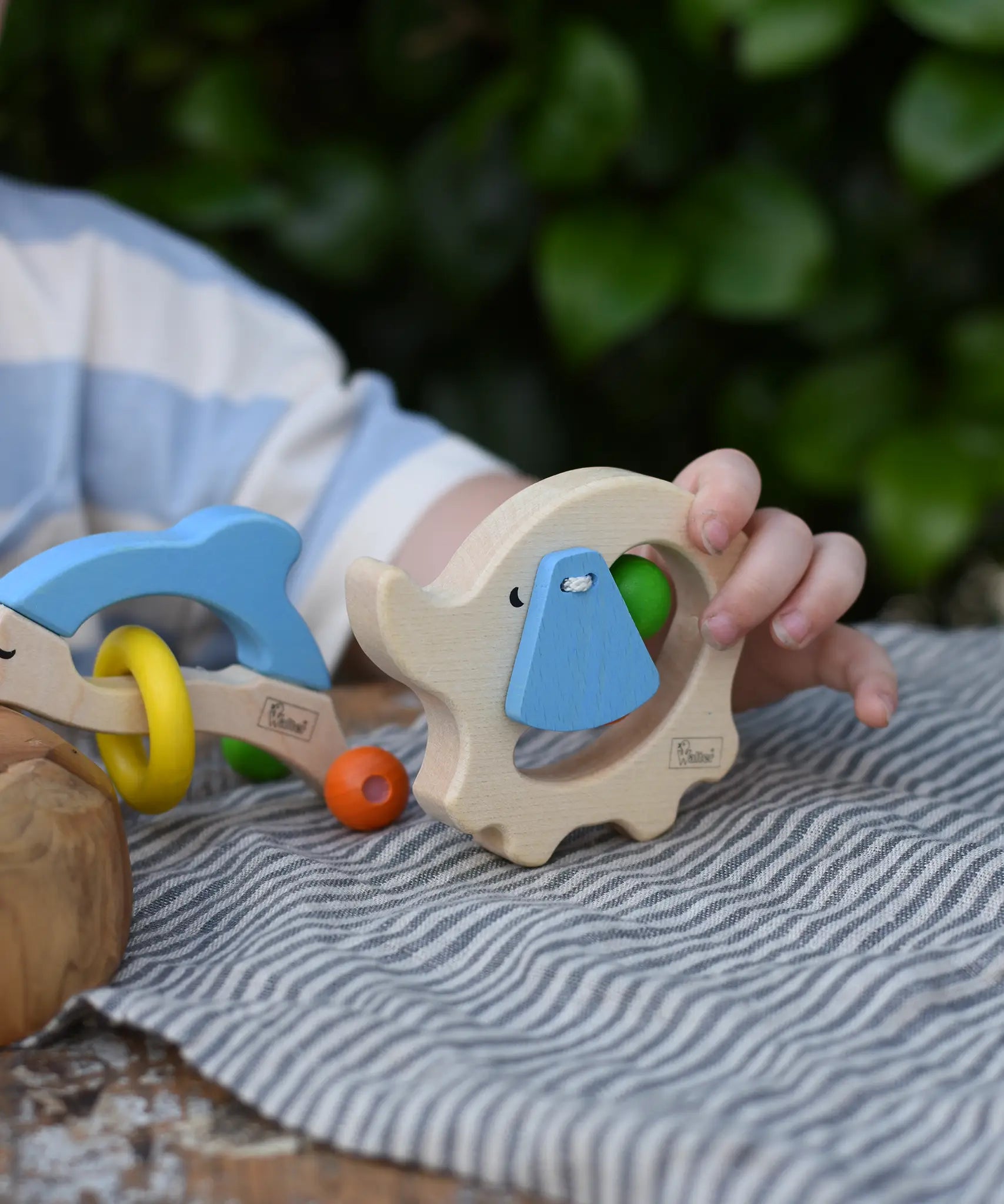 Child holding the back of the Nic elephant grasper wooden baby toy.