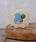 Nic elephant grasper wooden baby toy placed on a wooden surface. A light wood elephant body with blue ears and two green and orange beads inside. 