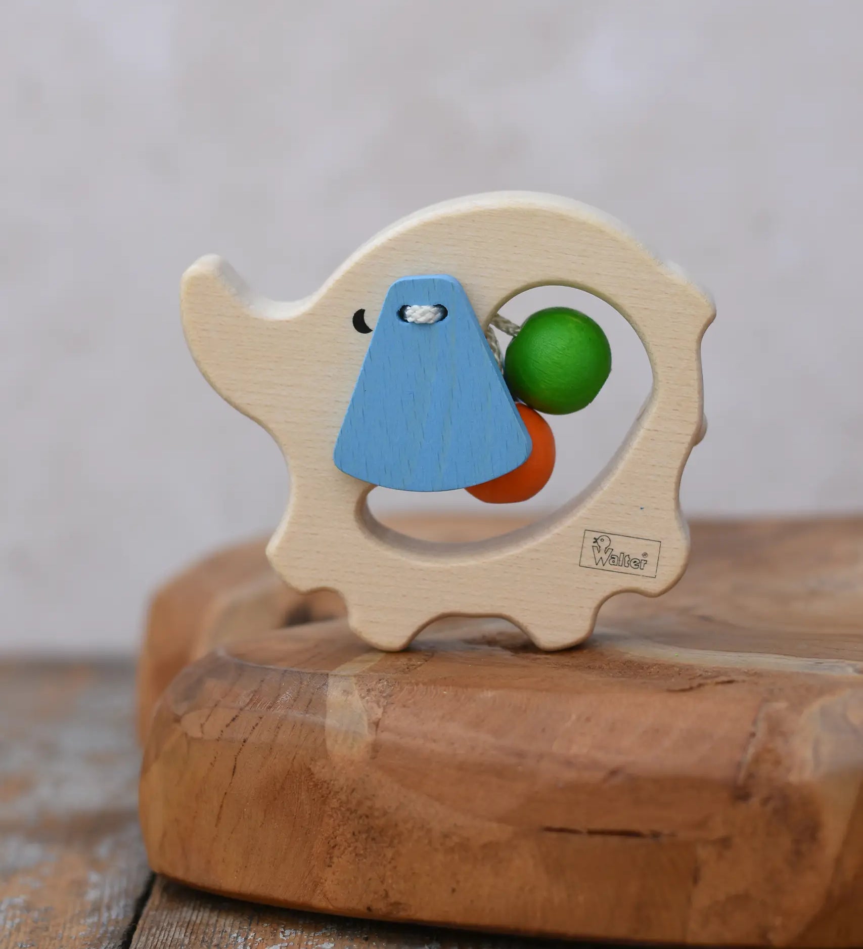 Nic elephant grasper wooden baby toy placed on a wooden surface. A light wood elephant body with blue ears and two green and orange beads inside. 