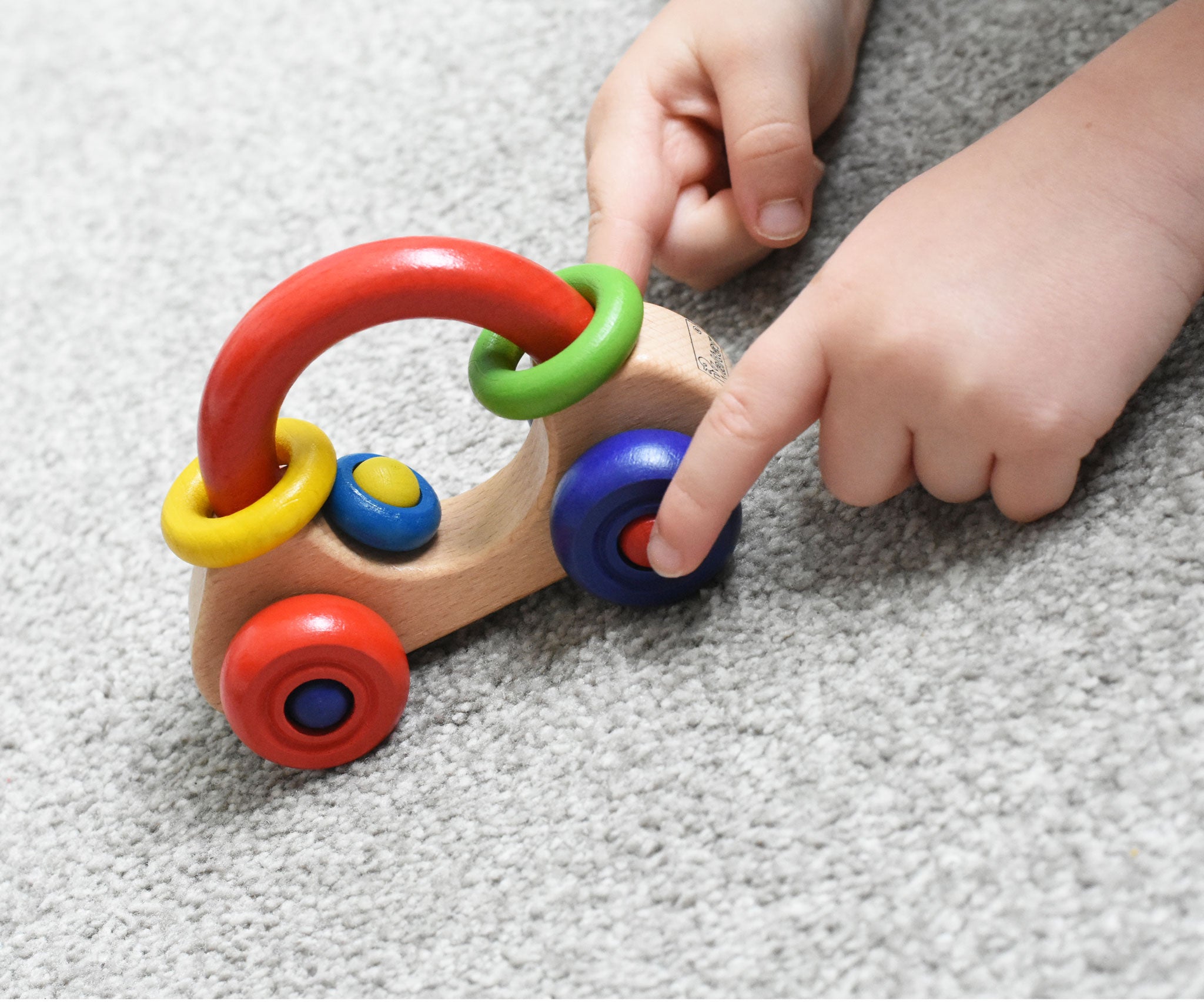 A close up of a child's hand playing with a Nic First Wooden Car - Baby Push-Along Toy.