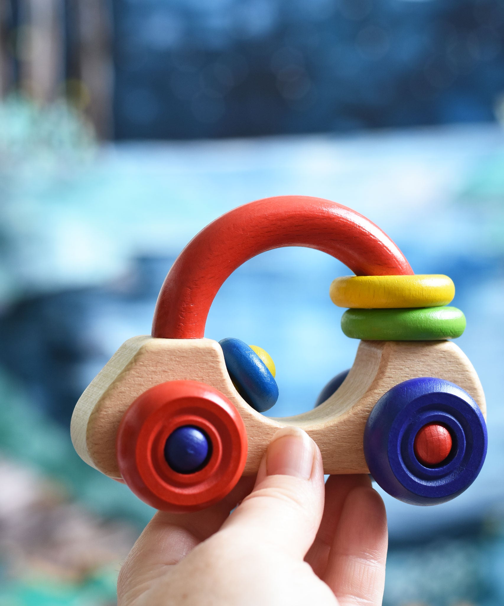 An adult's hand holding up a Nic First Wooden Car - Baby Push-Along Toy.
