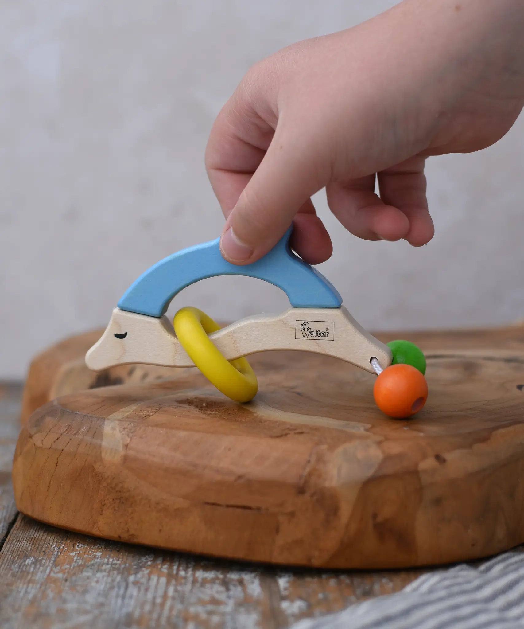 Child's hand reaching for the Nic dolphin wooden baby grasping toy.