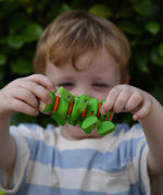 Child holding the Nic Willy the centipede green wooden baby toy up in front of their face.