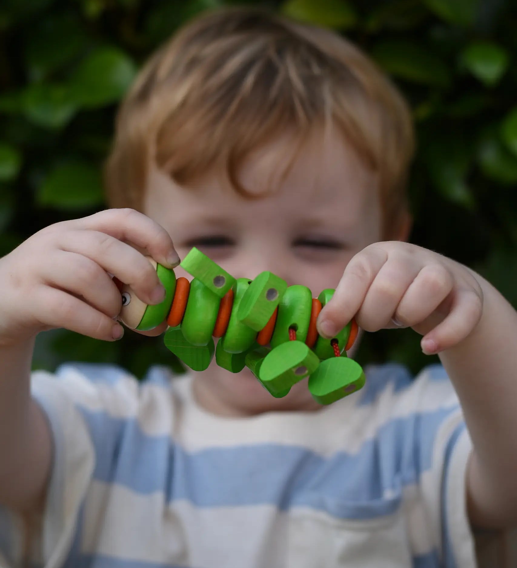 Child holding the Nic Willy the centipede green wooden baby toy up in front of their face.