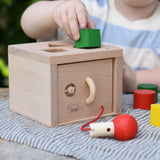 Nic lock a bloc wooden shape sorter toy, child is placing one of the green blocks into the slot at the top. 