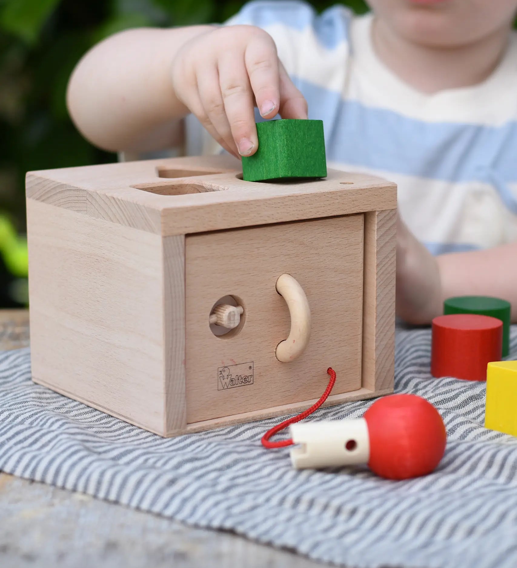 Nic lock a bloc wooden shape sorter toy, child is placing one of the green blocks into the slot at the top. 