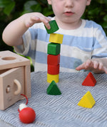Child stacking the green yellow and red blocks from the Nic lock a bloc wooden shape sorter toy on top of each other.