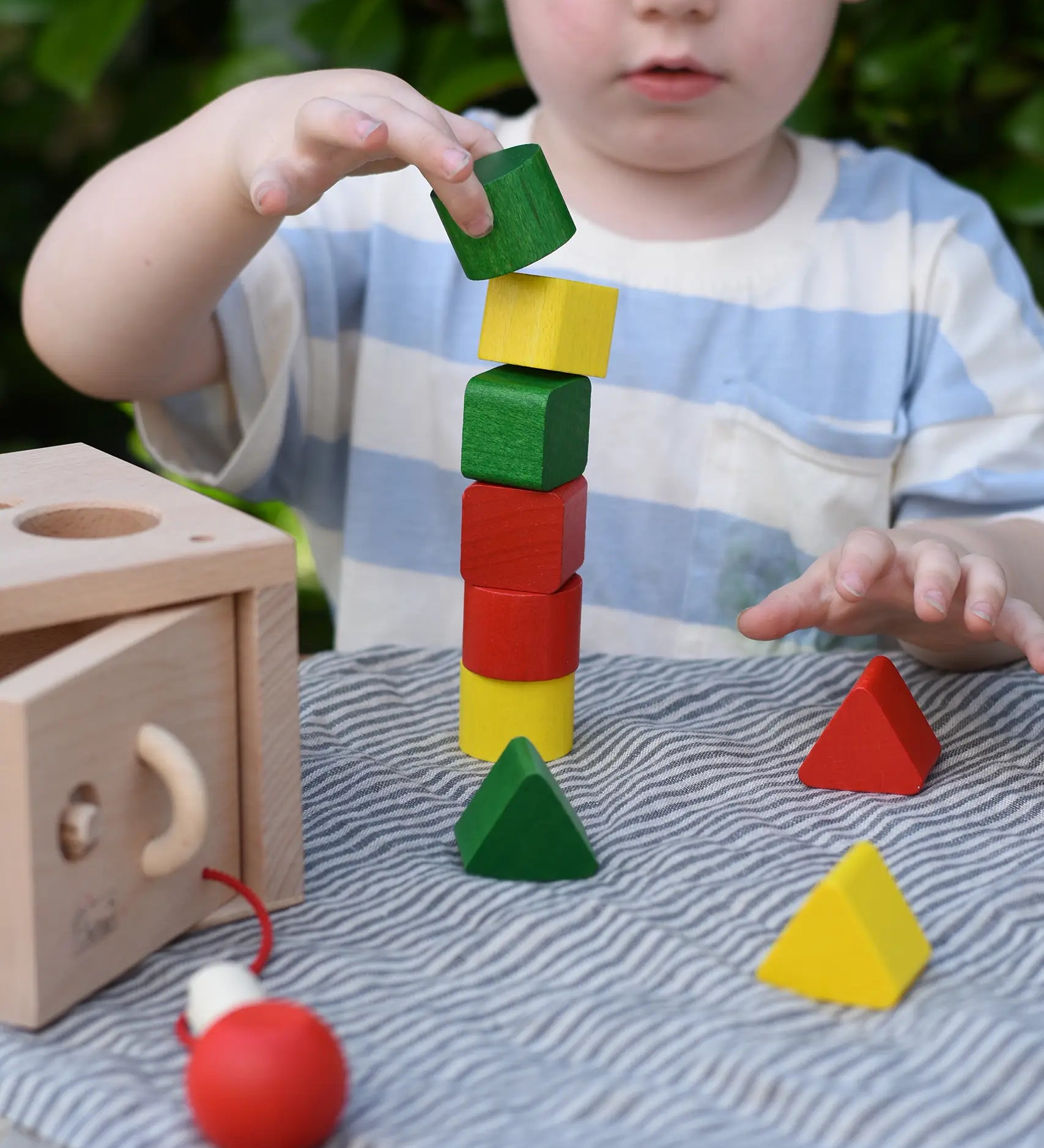 Child stacking the green yellow and red blocks from the Nic lock a bloc wooden shape sorter toy on top of each other.