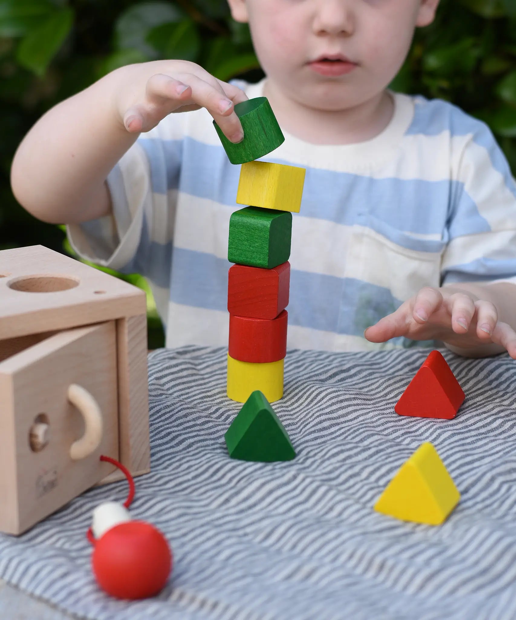 Child stacking the green yellow and red blocks from the Nic lock a bloc wooden shape sorter toy on top of each other.