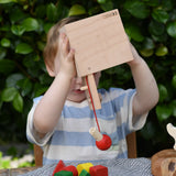 Child holding the Nic lock a bloc wooden shape sorter toy upside down with the door open and emptying the blocks from inside. 