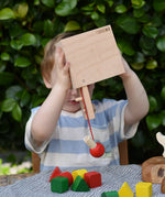 Child holding the Nic lock a bloc wooden shape sorter toy upside down with the door open and emptying the blocks from inside. 