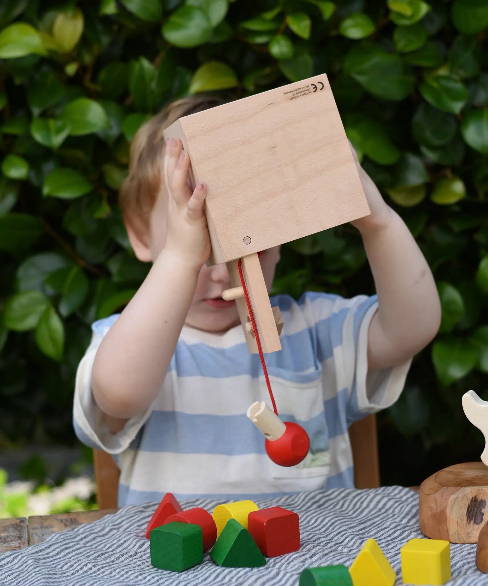 Child holding the Nic lock a bloc wooden shape sorter toy upside down with the door open and emptying the blocks from inside. 