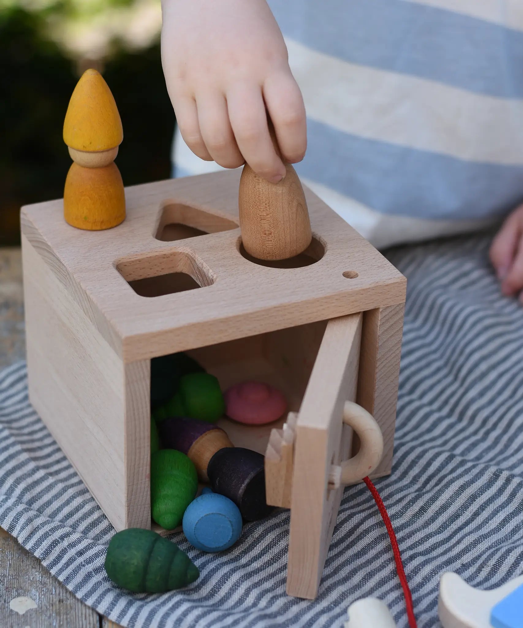 Child posting Grapat Nins and mandala pieces through the slots on the Nic lock a bloc wooden shape sorter toy.