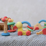 Collection of Nic organic wooden baby toys placed on a striped cloth. Spinning carousel rattle, push ducks and keys placed next to each other with others in the background.