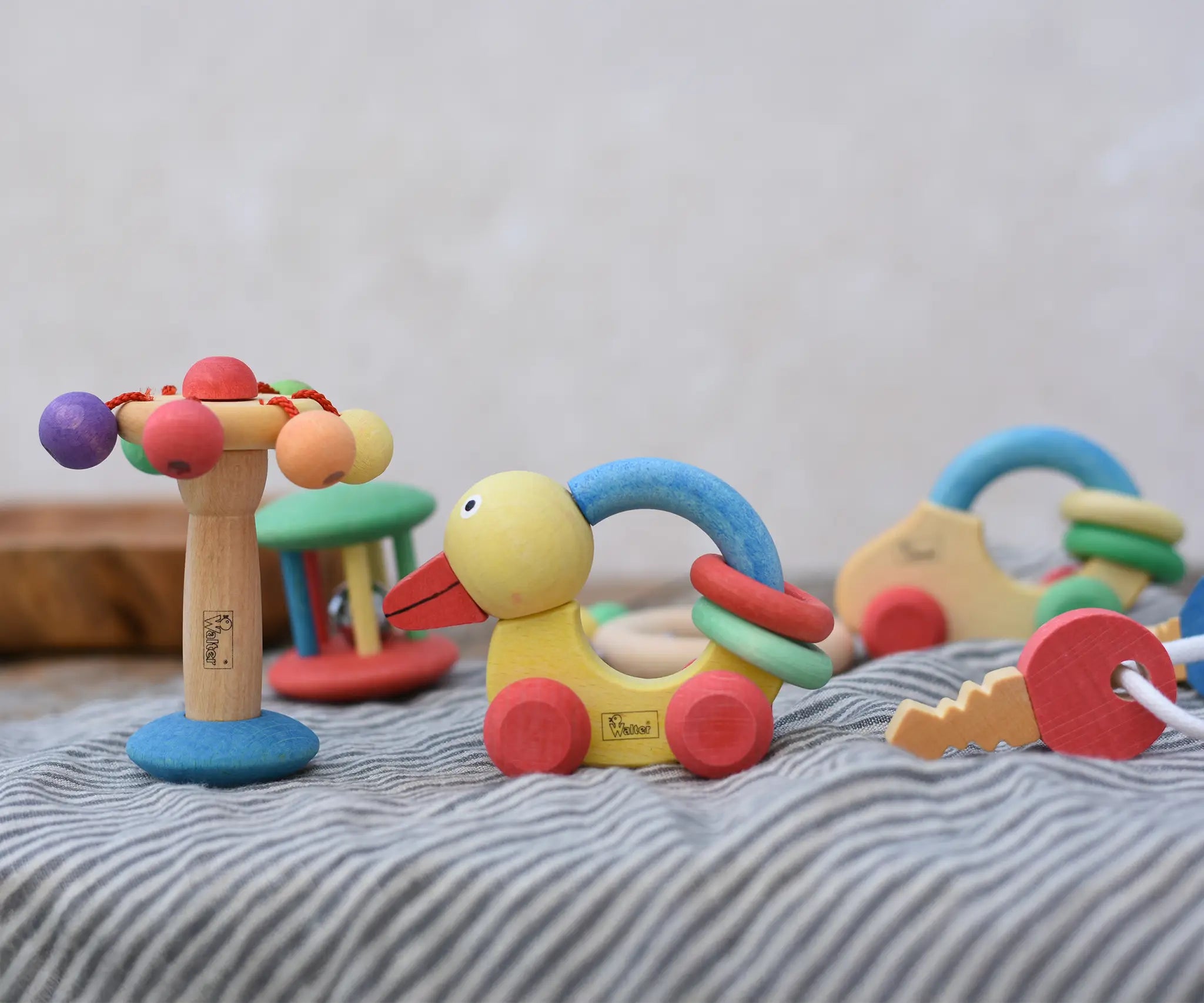 Collection of Nic organic wooden baby toys placed on a striped cloth. Spinning carousel rattle, push ducks and keys placed next to each other with others in the background.