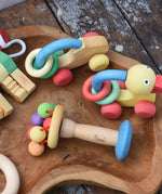 Nic organic carousel rattle spinning baby grasping toy placed on a wooden dish with other baby toys from the Nic organic collection by Gluckskafer.