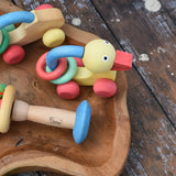 Nic organic grip duck wooden push along baby toy placed on a wooden dish next to other toys from the Gluckskafer Nic organic baby toy collection. 