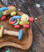 Nic organic grip duck wooden push along baby toy placed on a wooden dish next to other toys from the Gluckskafer Nic organic baby toy collection. 