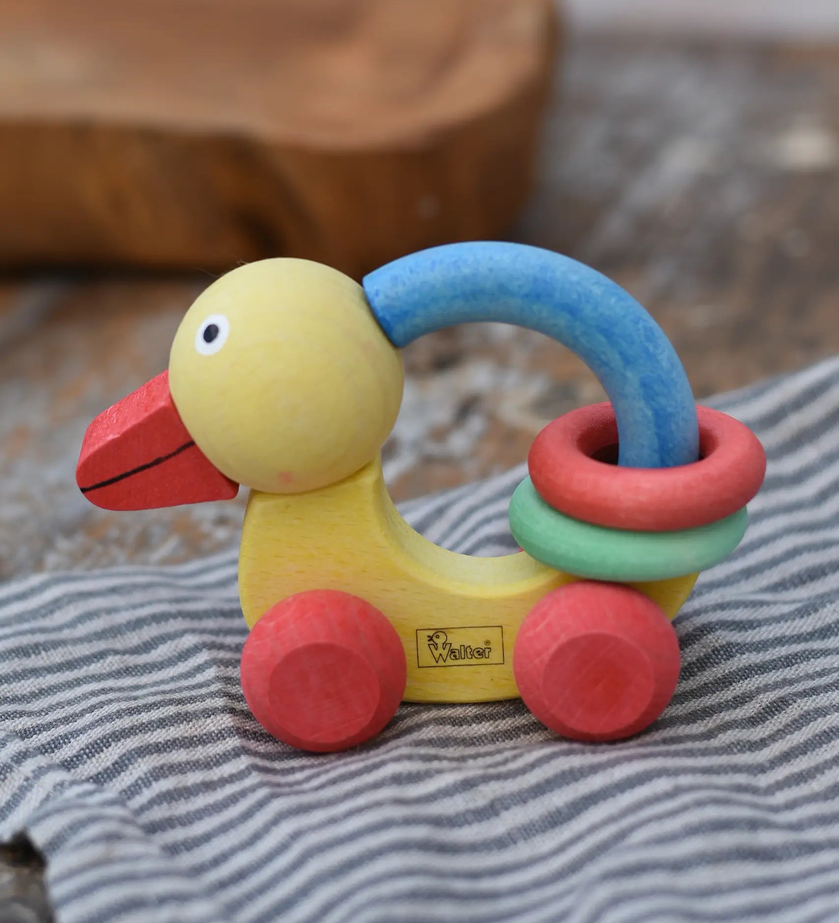Nic organic grip duck wooden push along baby toy placed on a striped grey cloth.