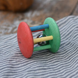Nic organic jingle bell wooden roller baby toy placed on a striped grey cloth 