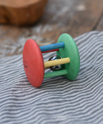 Nic organic jingle bell wooden roller baby toy placed on a striped grey cloth 