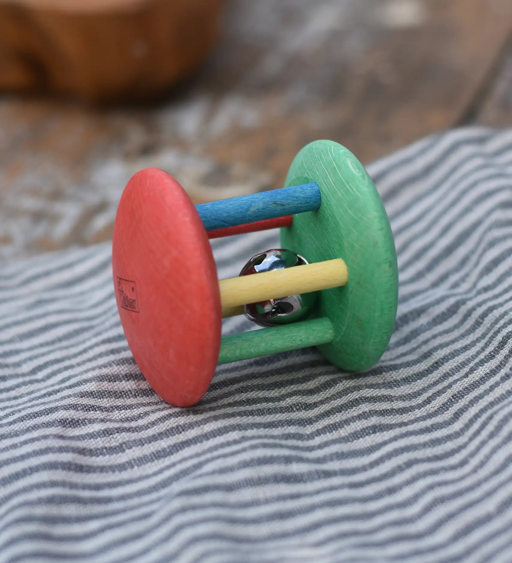 Nic organic jingle bell wooden roller baby toy placed on a striped grey cloth 