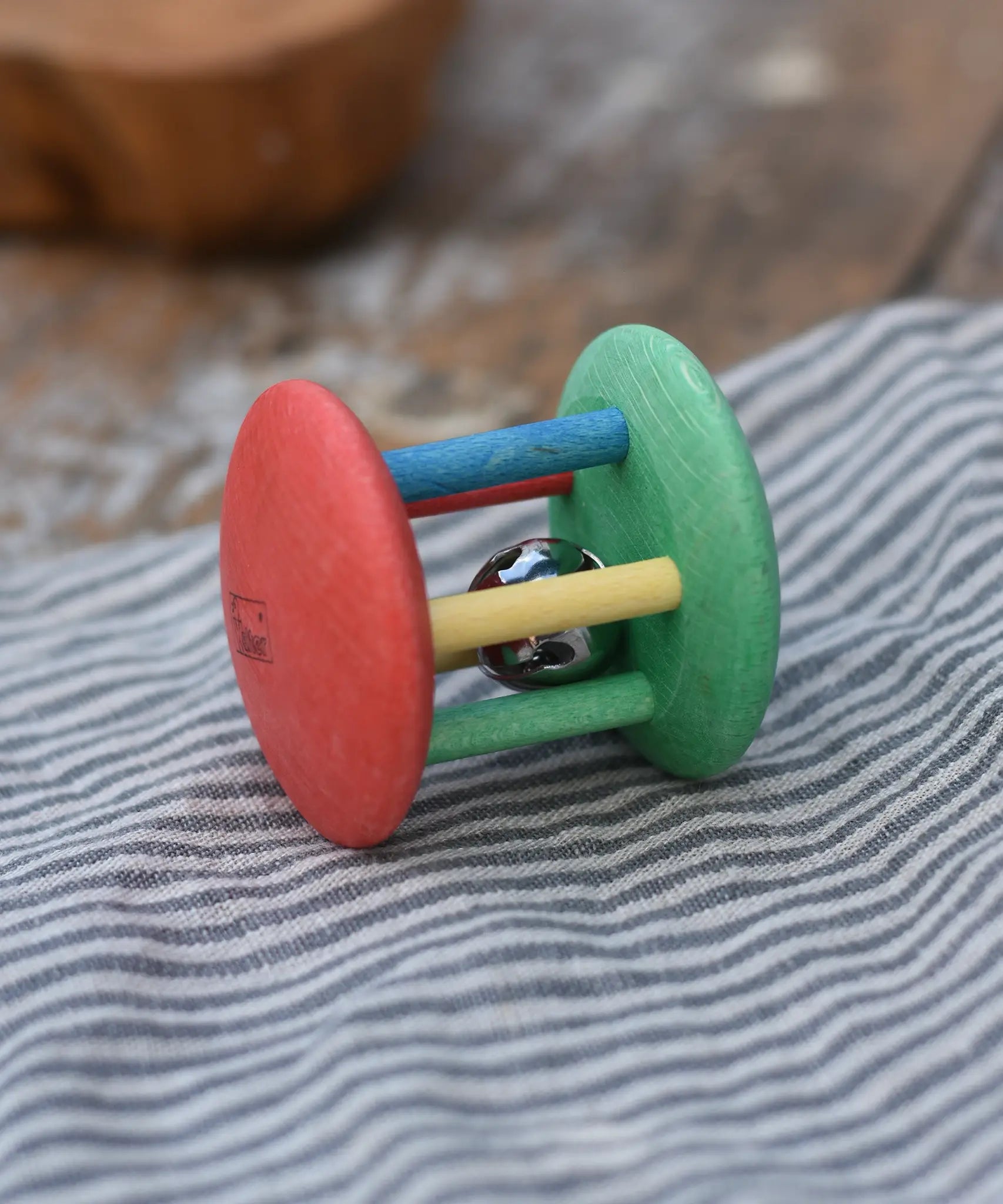 Nic organic jingle bell wooden roller baby toy placed on a striped grey cloth 