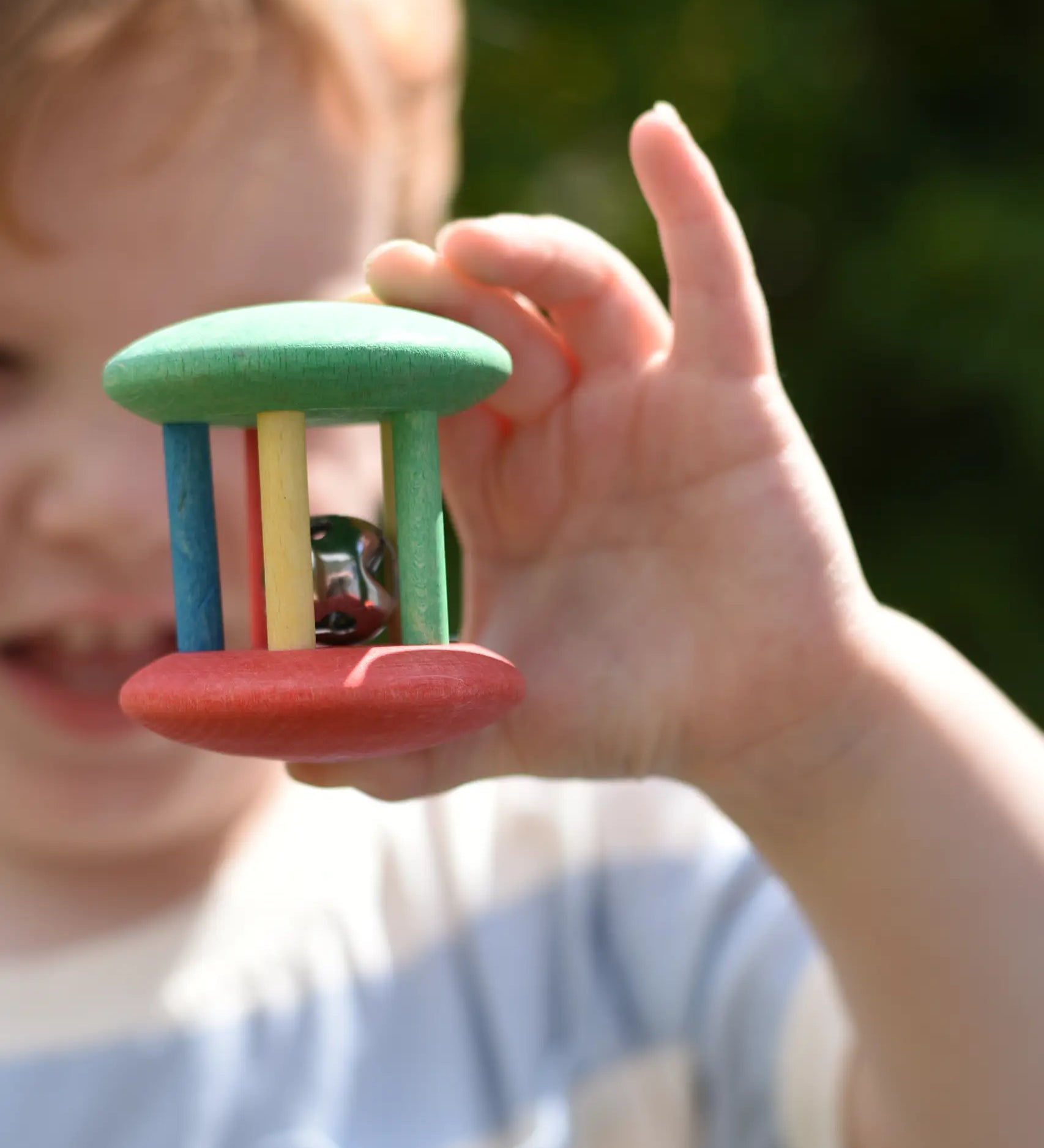 Nic organic jingle bell wooden roller baby toy in a child's hand. 