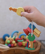 Nic organic wooden grasping keyring set in  a child's hand held up by the yellow key. 
