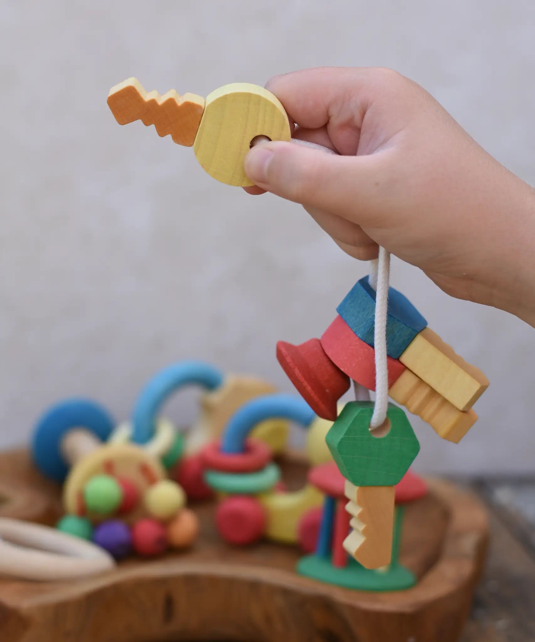 Nic organic wooden grasping keyring set in  a child's hand held up by the yellow key. 