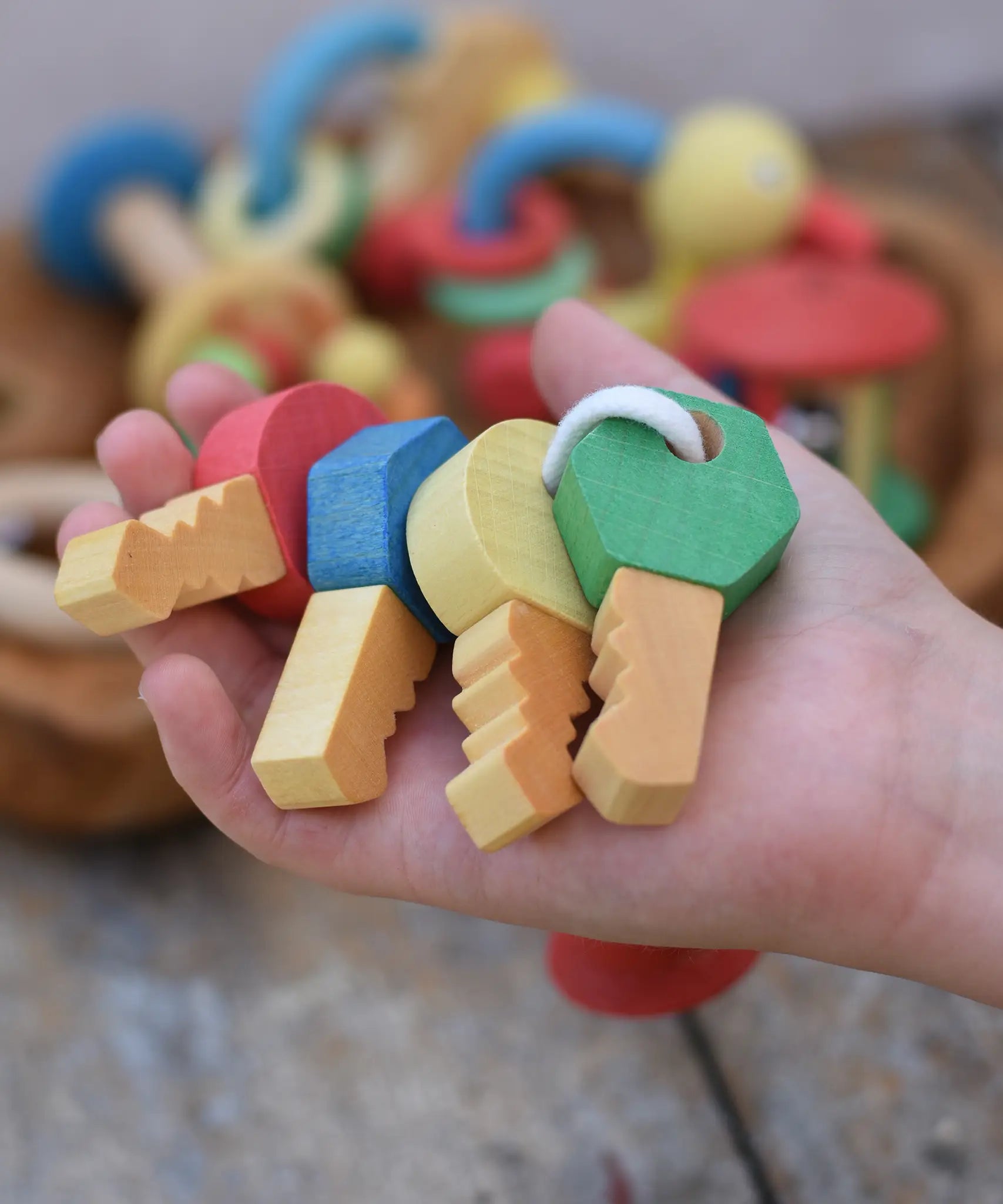 Nic organic wooden grasping keyring set in a child's hand. Four wooden keys on a rope keyring.