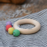 Nic organic teething ring wooden baby toy placed on a striped grey cloth. 