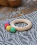 Nic organic teething ring wooden baby toy placed on a striped grey cloth. 