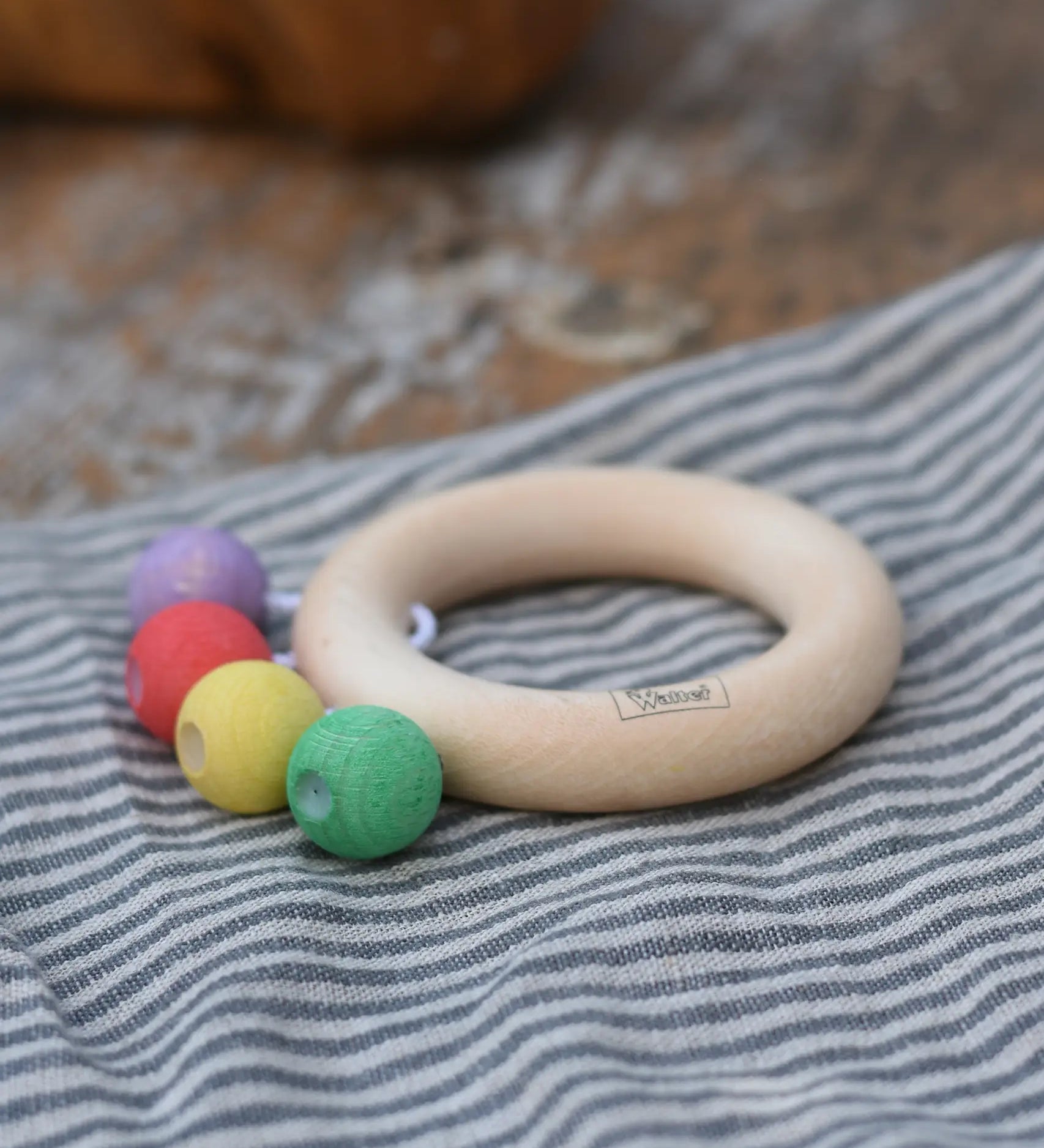 Nic organic teething ring wooden baby toy placed on a striped grey cloth. 