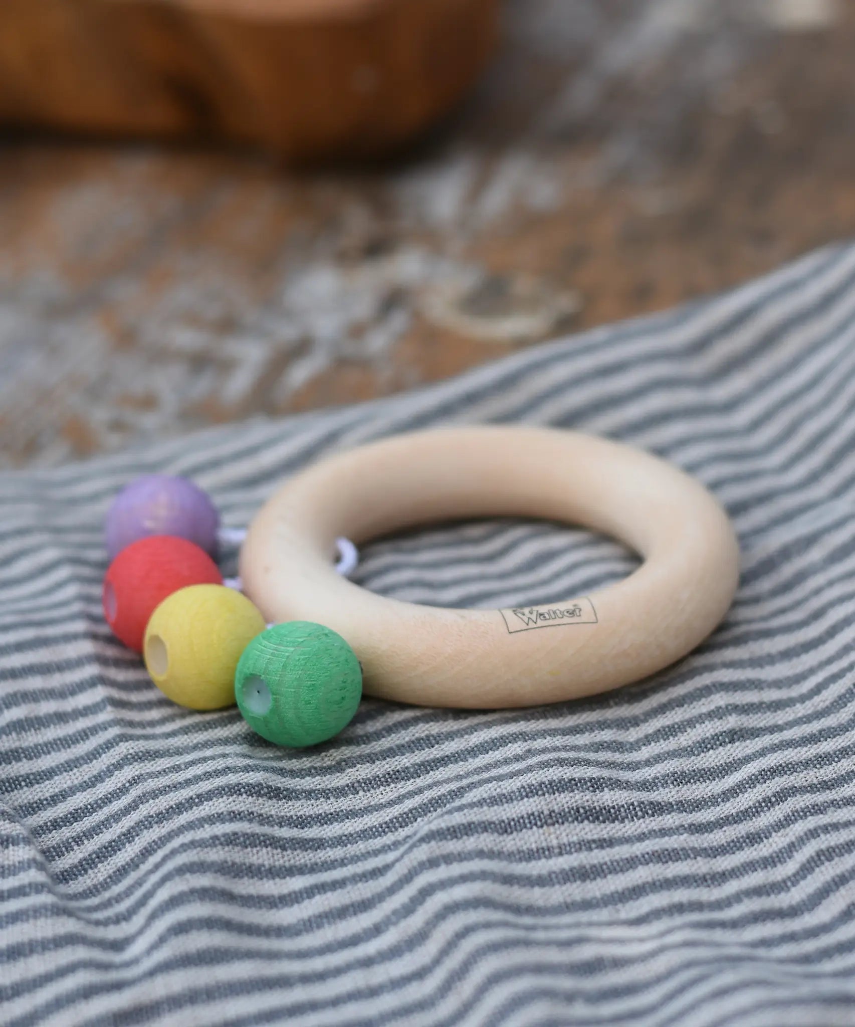 Nic organic teething ring wooden baby toy placed on a striped grey cloth. 