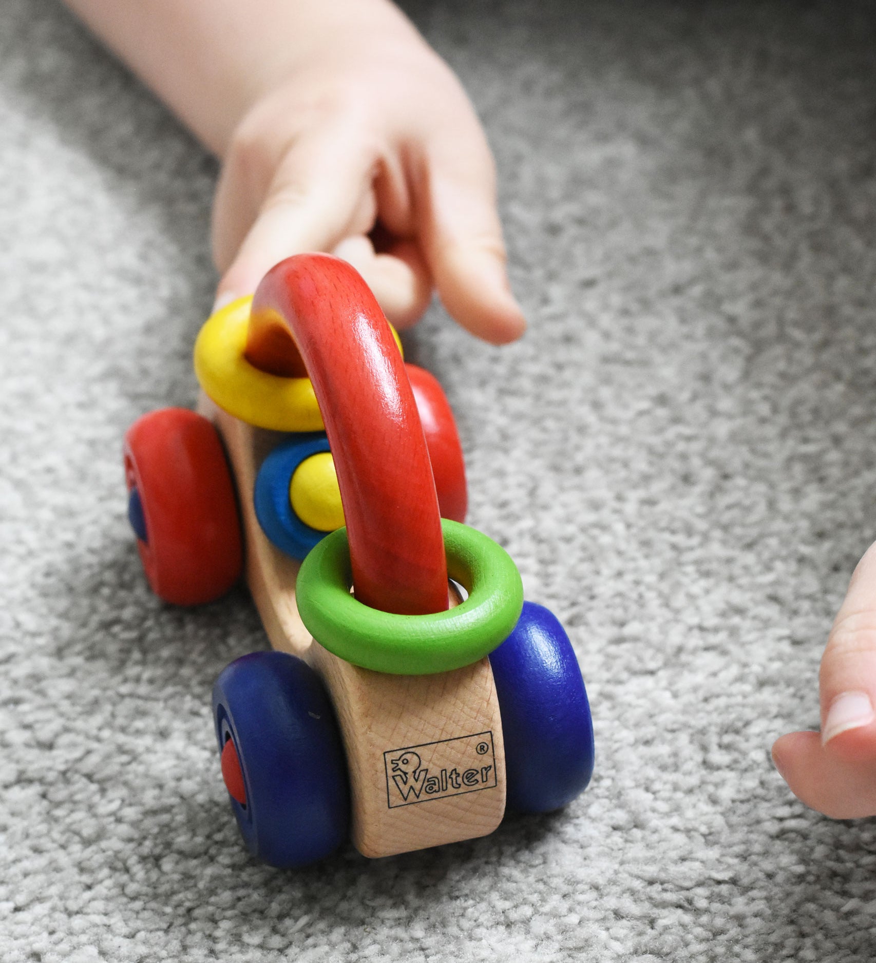 A close up of the Nic First Wooden Car Baby Push-Along Toy being pushed by a child's hand. 