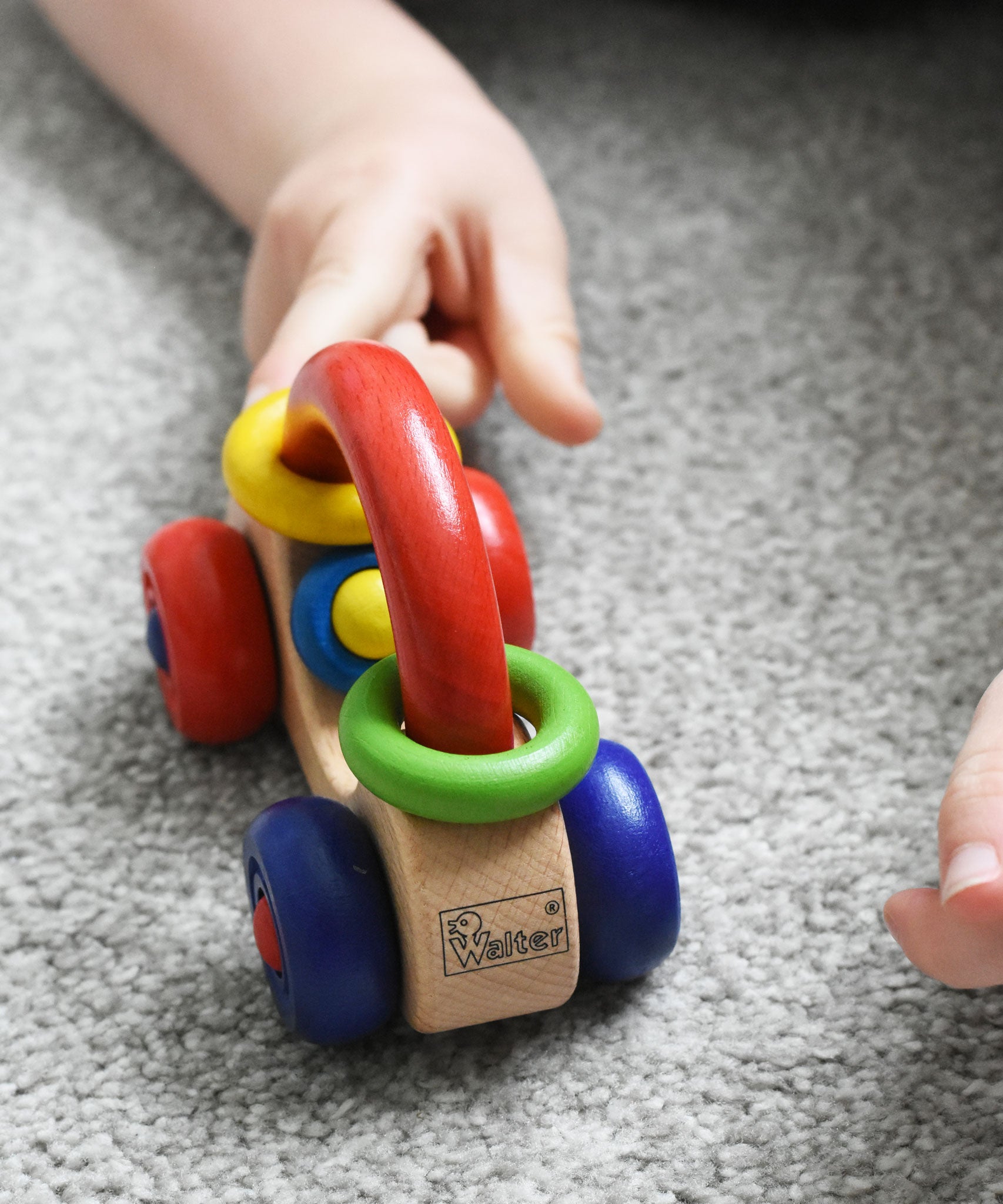 A close up of the Nic First Wooden Car Baby Push-Along Toy being pushed by a child's hand. 