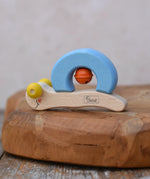 Nic snail baby grasping toy. A light wood and blee wooden toy snail with yellow beads for eyes and an orange bell. 