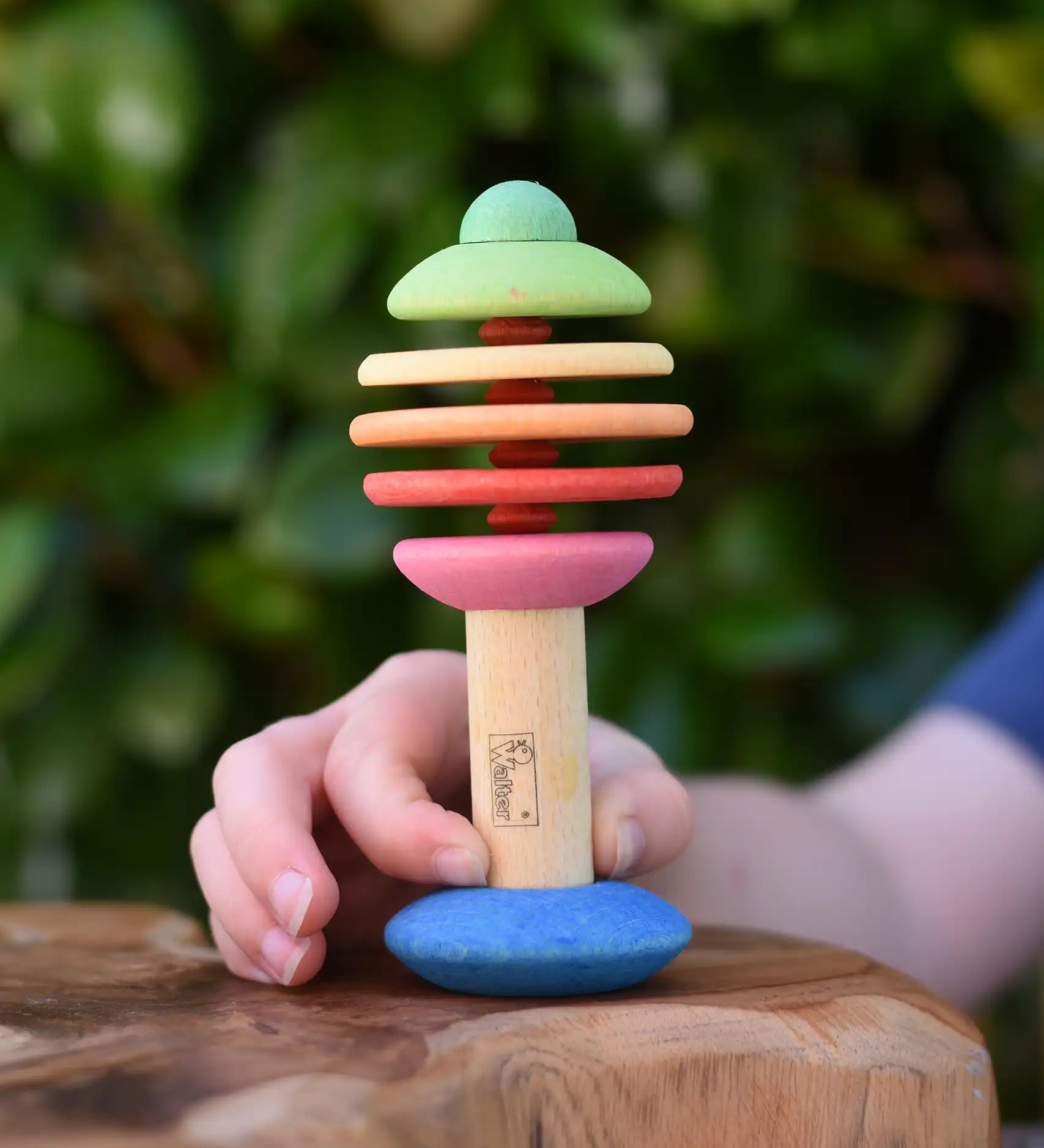 Child holding the Nic Toys bio wooden rattling tree baby toy. Coloured disks for making a noise and a wooden handle for grip.