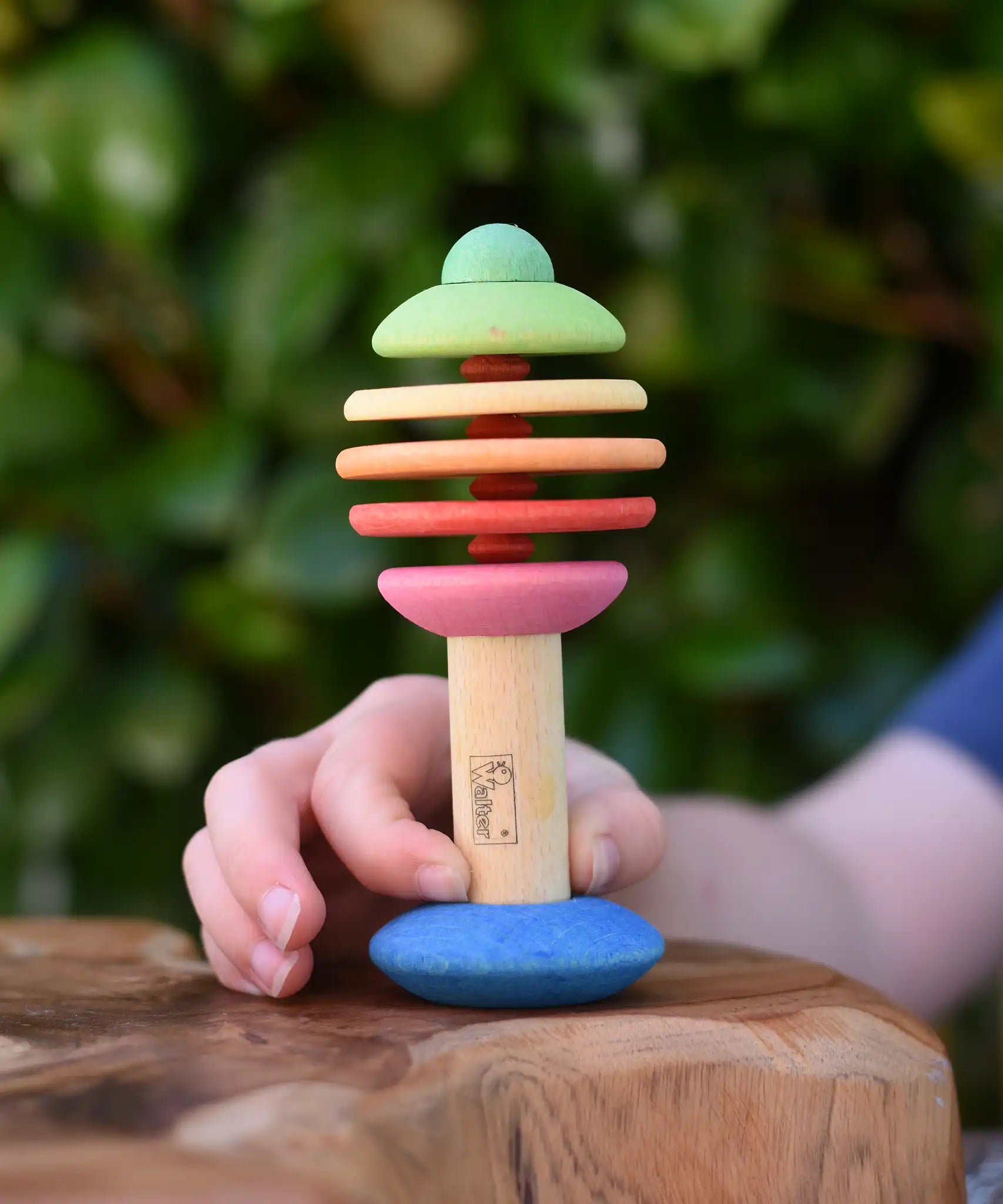 Child holding the Nic Toys bio wooden rattling tree baby toy. Coloured disks for making a noise and a wooden handle for grip.