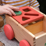 Child placing a green cylinder block into the slot on the Nic wooden carriage shape sorter pull along toy. 8 wooden blocks in various shapes and colours.