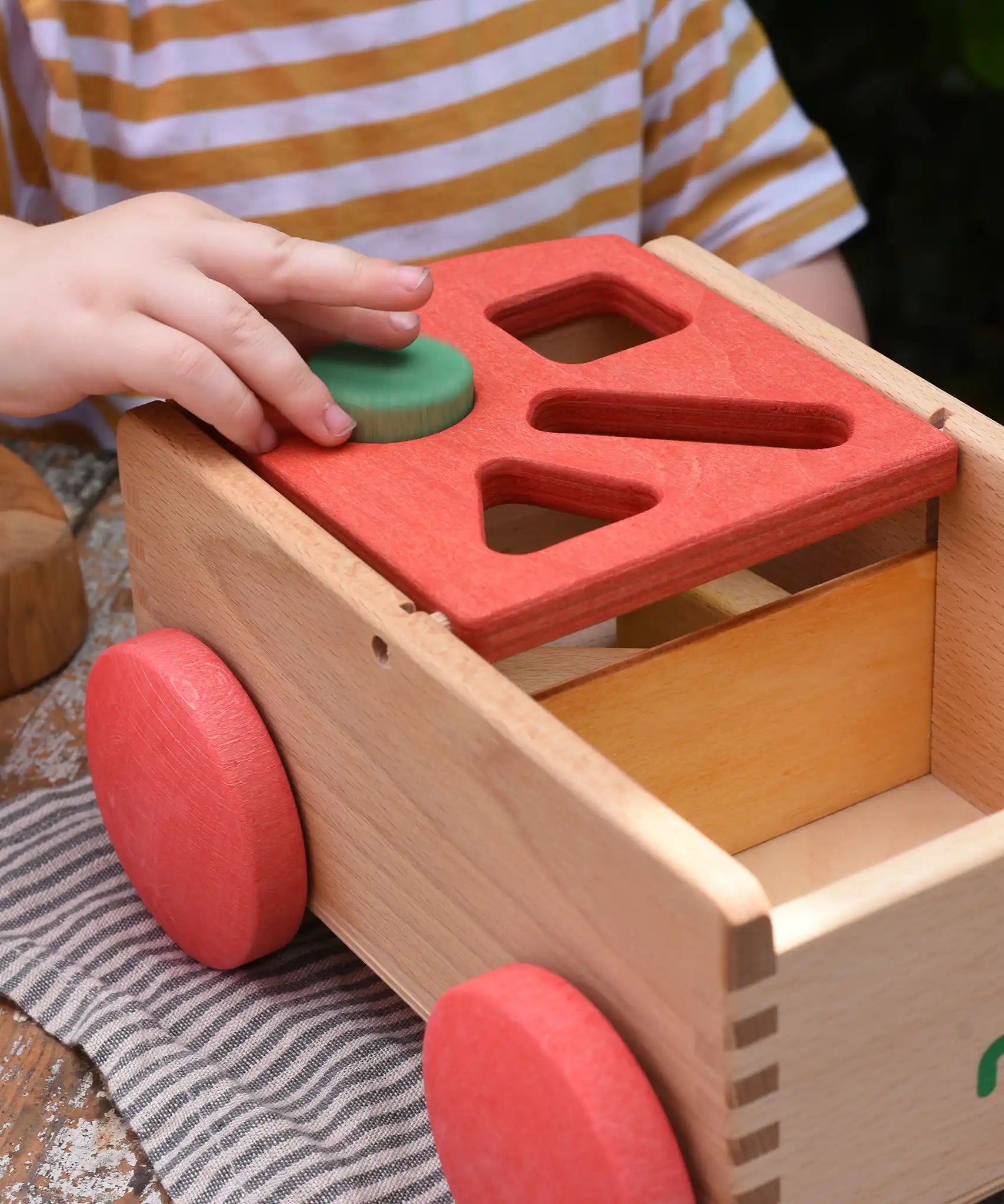 Child placing a green cylinder block into the slot on the Nic wooden carriage shape sorter pull along toy. 8 wooden blocks in various shapes and colours.