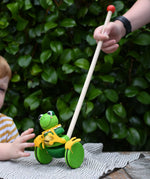 Child pushing the Nic Toys frog king push along toy. Green frog with yellow felt details and gold bell. 