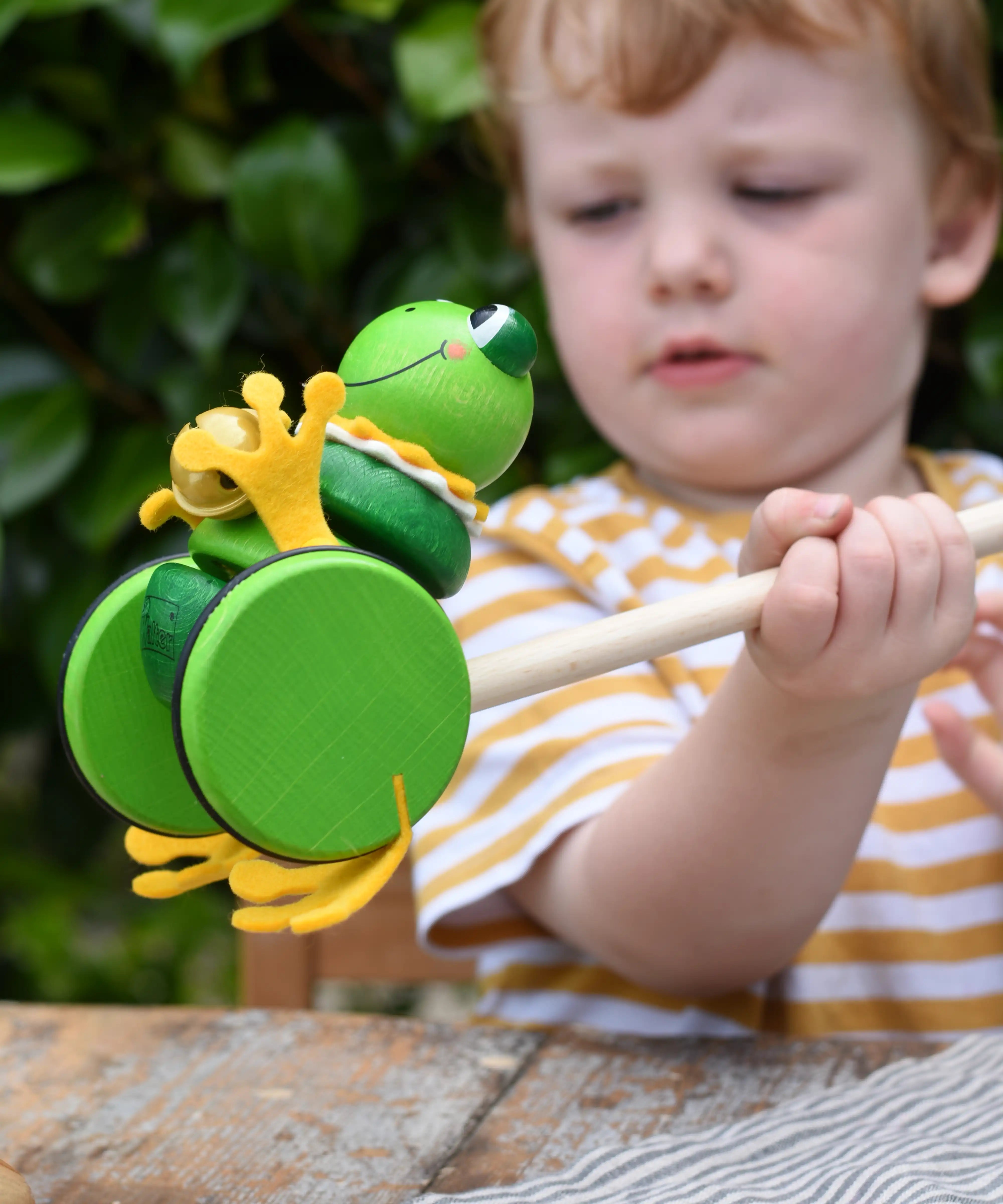 Child holding the Nic Toys frog king push along toy. Green frog with yellow felt details and gold bell. 