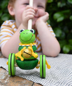 Child holding the stick on the Nic Toys frog king push along toy. Green frog with yellow felt details and gold bell. 