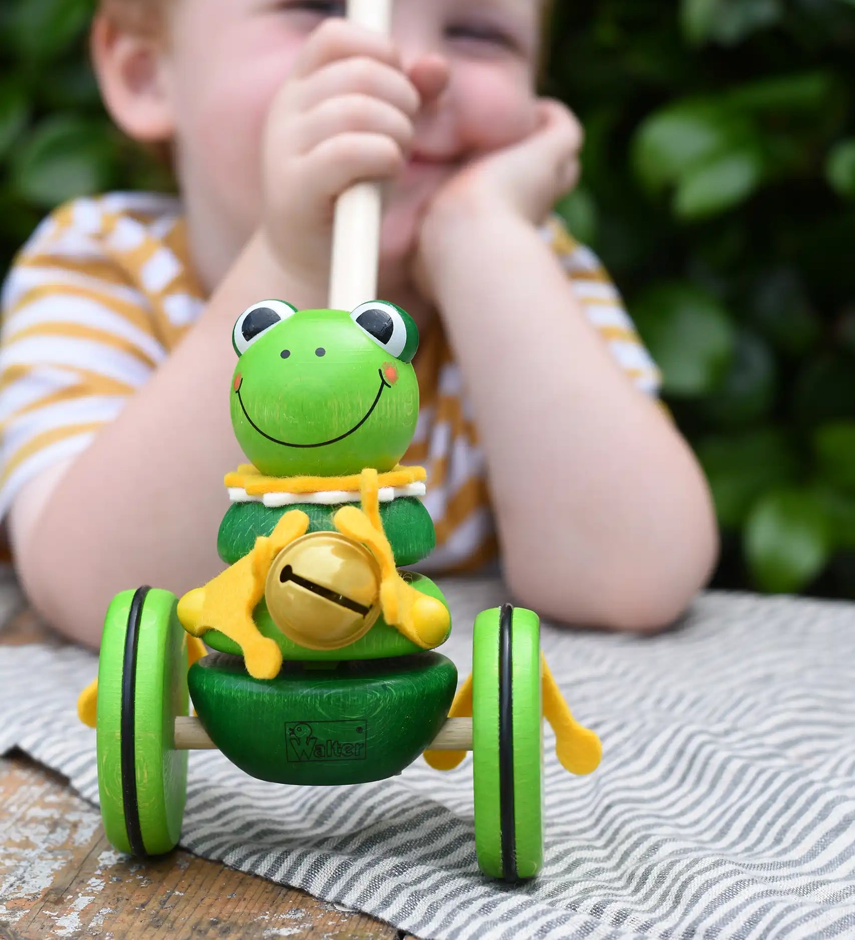 Child holding the stick on the Nic Toys frog king push along toy. Green frog with yellow felt details and gold bell. 