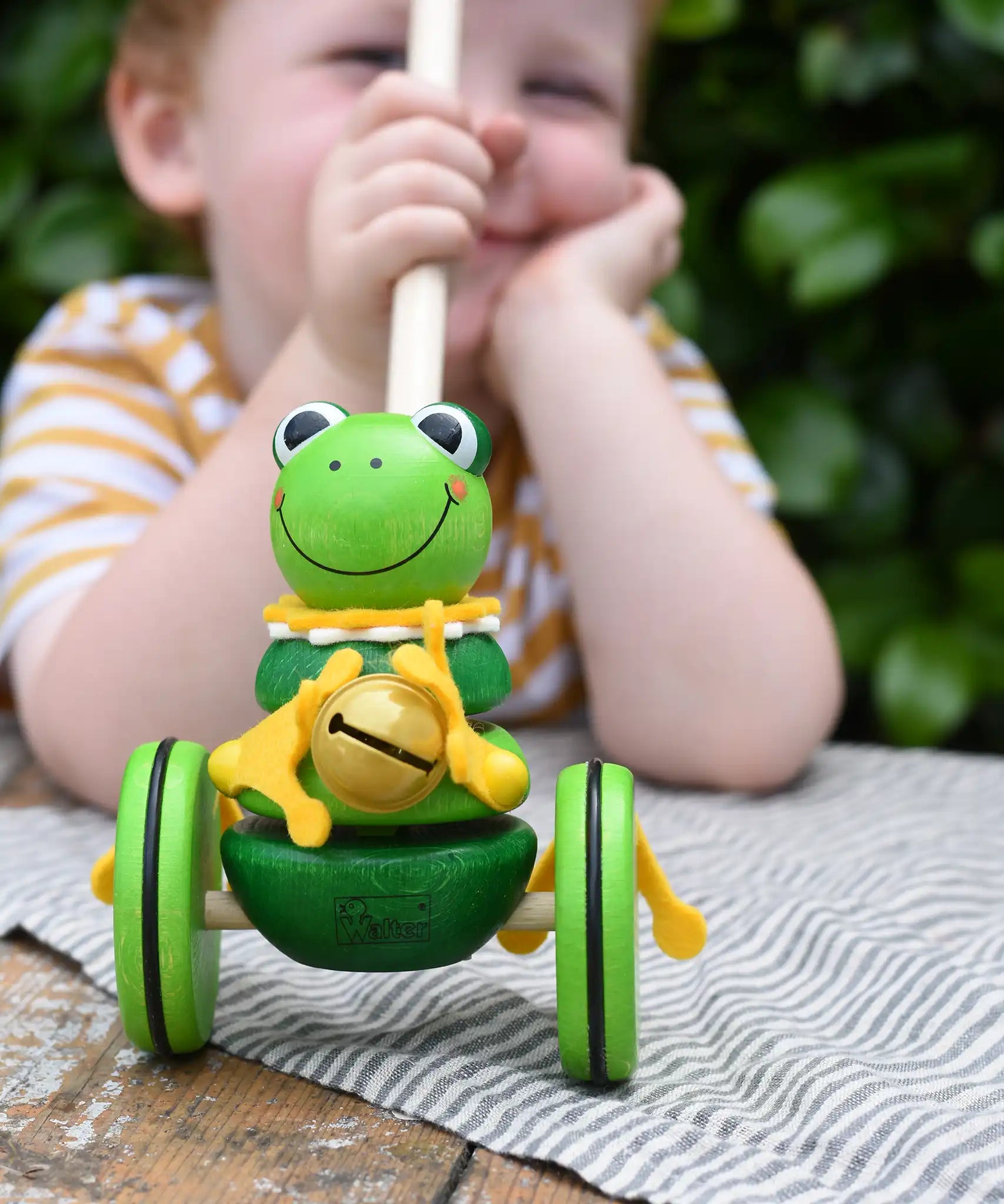 Child holding the stick on the Nic Toys frog king push along toy. Green frog with yellow felt details and gold bell. 