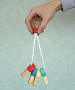 A adult hand holding the Nic Toys wooden grasping keyring set available at Babipur against a green decorative background.