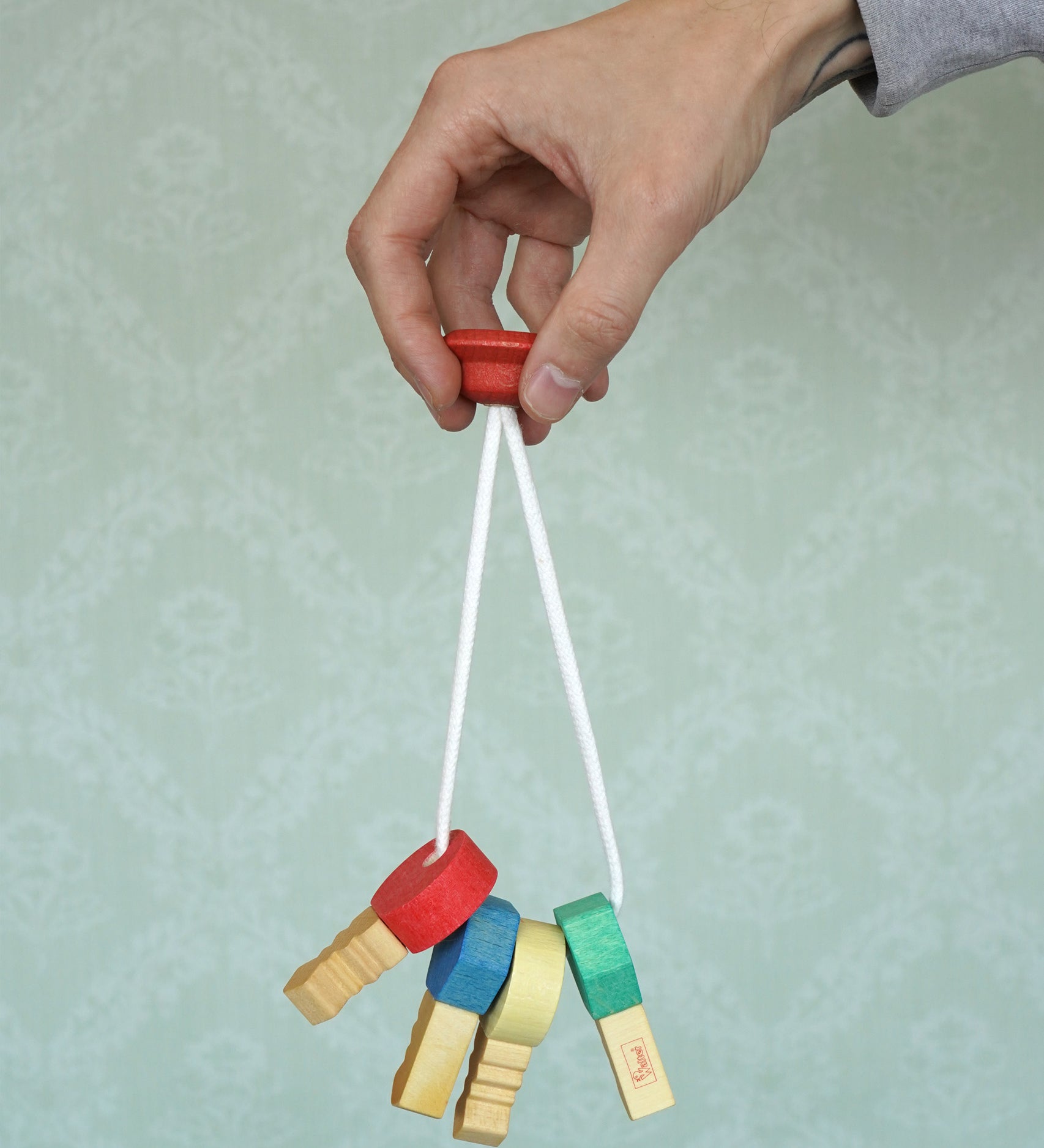 A adult hand holding the Nic Toys wooden grasping keyring set available at Babipur against a green decorative background.